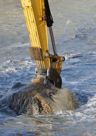 Excavator bucket dredging sand and gravel from the seafront