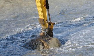Excavator bucket dredging sand and gravel from the seafront